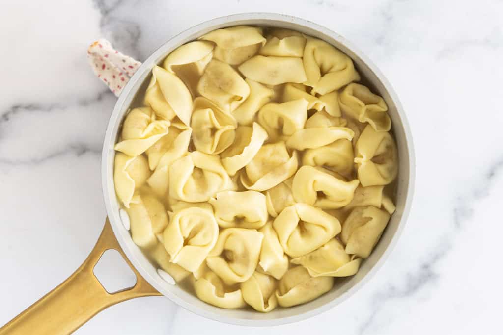 Tortellini being cooked in pan in broth.