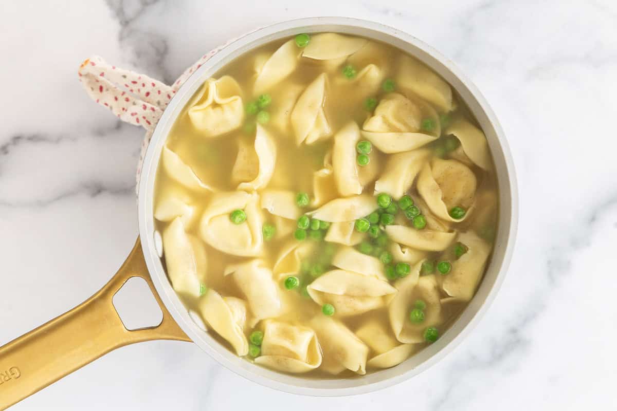 Tortellini and peas in broth in pot.