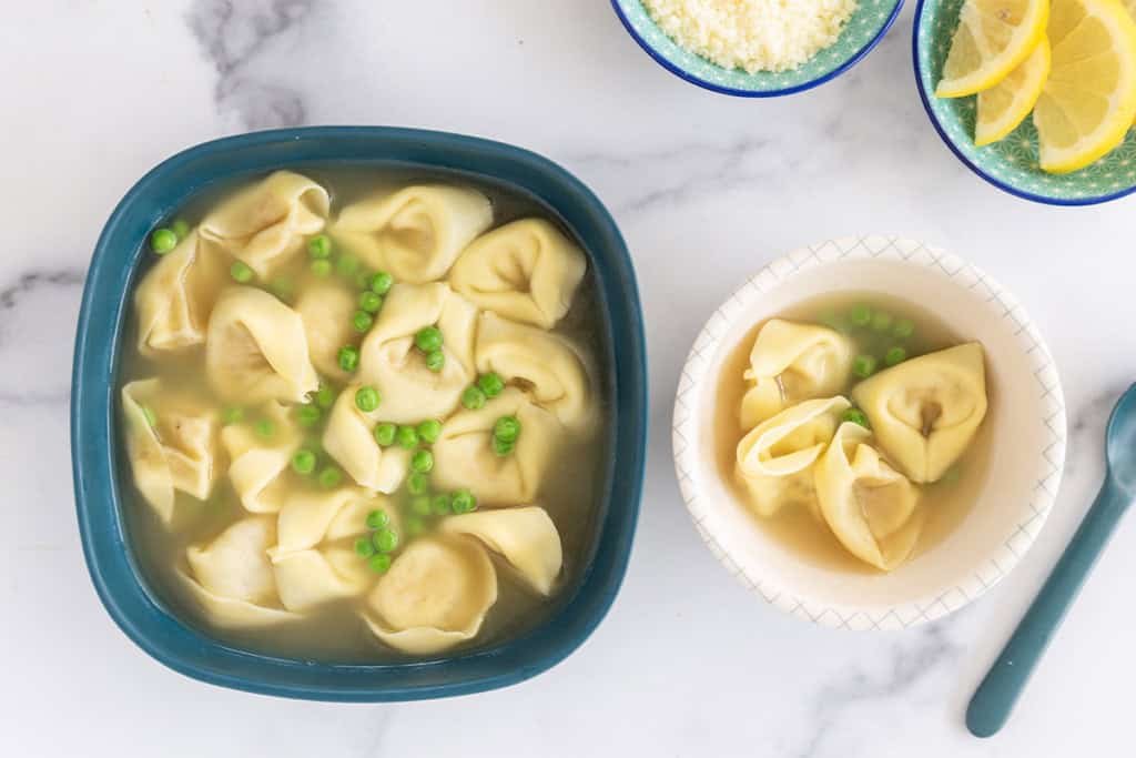 Tortellini in broth in two bowls with spoons.