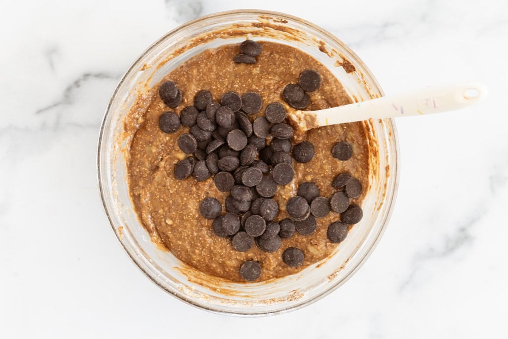 Adding chocolate chips to batter for chocolate peanut butter muffins.