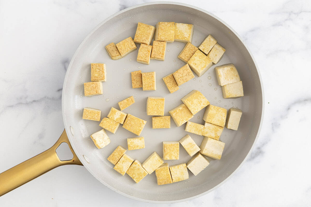 Tofu being fried in pan for green curry. 