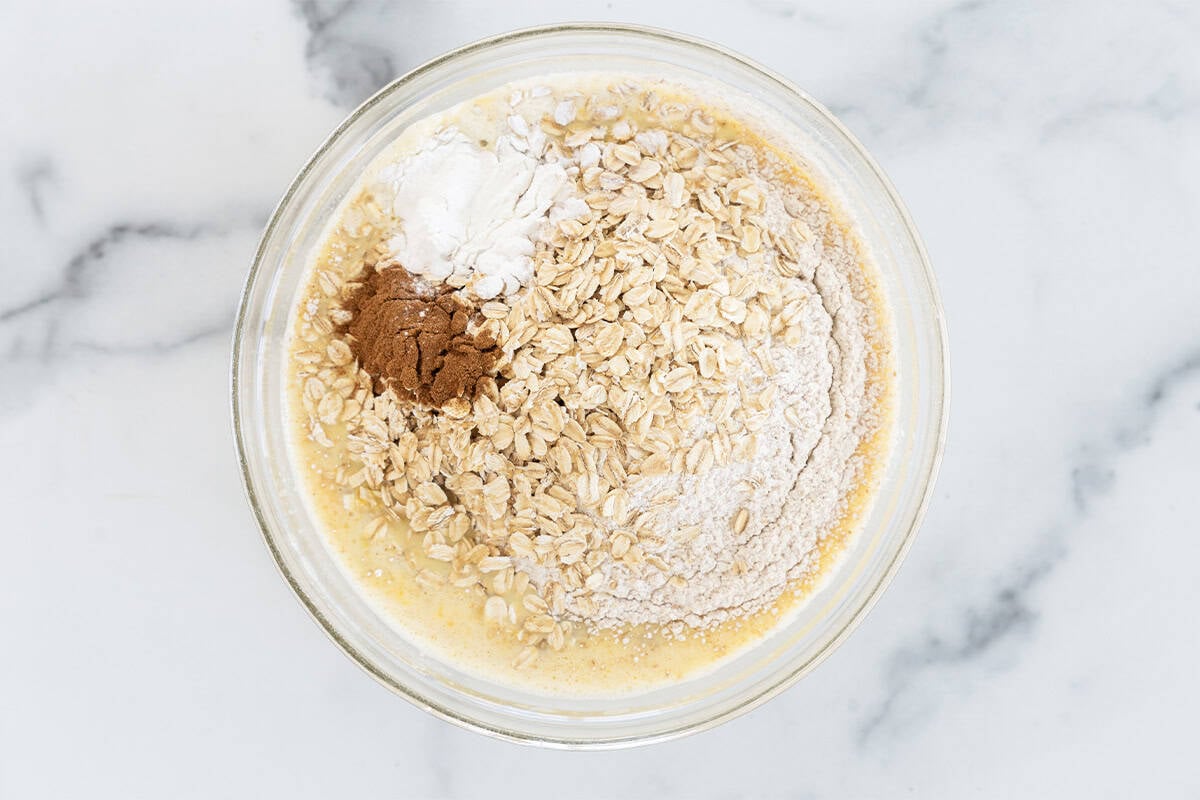 Ingredients for banana oatmeal pancakes in glass bowl before mixing.