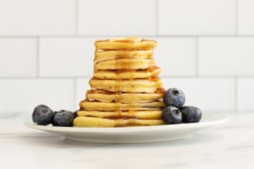 stack of pancakes with syrup dripping and berries on the side.