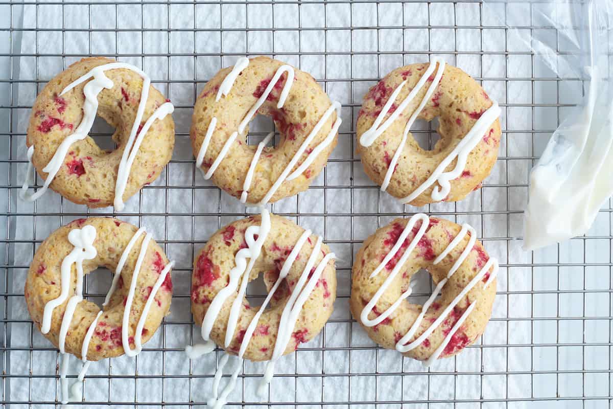 adding icing to baked raspberry donuts on wire rack.