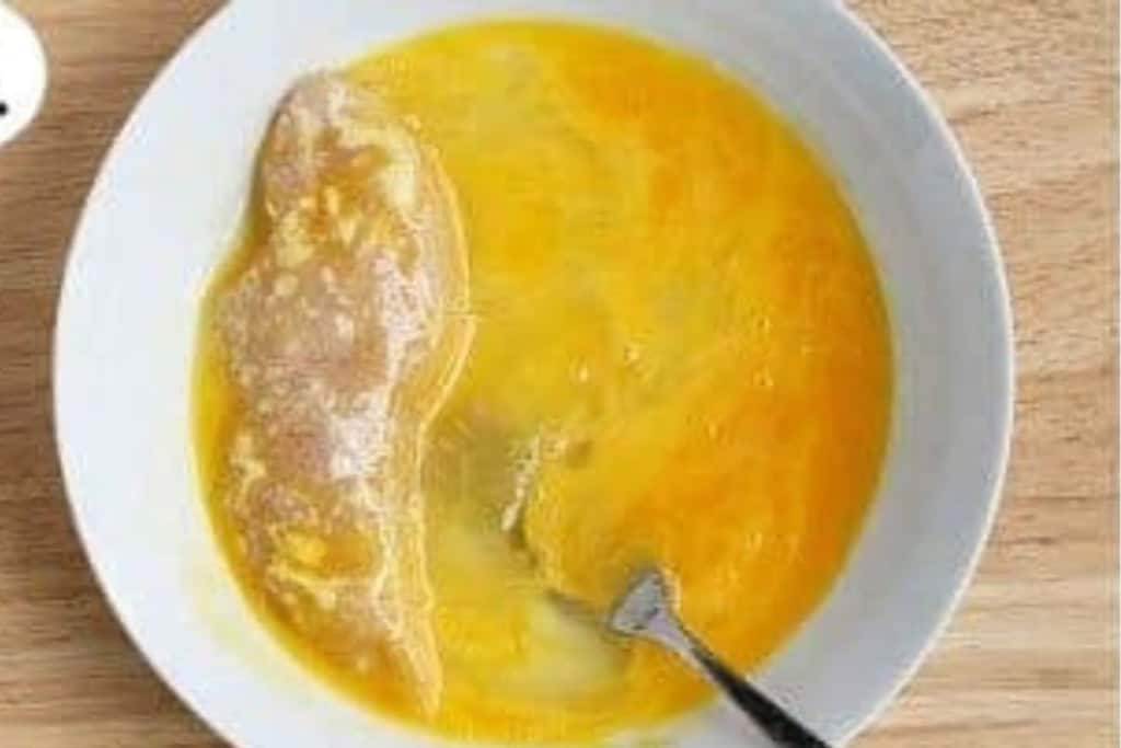 Chicken tender being dipped in egg.