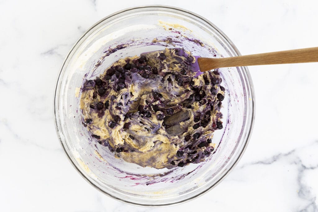 mixed blueberry yogurt muffin batter in glass bowl with spatula.