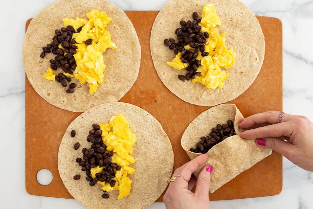 assembling breakfast burritos on cutting board.