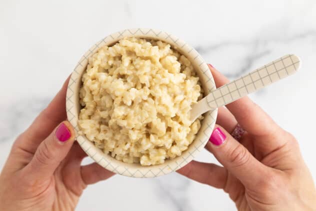cheesy rice in bowl with hands and pink nails.