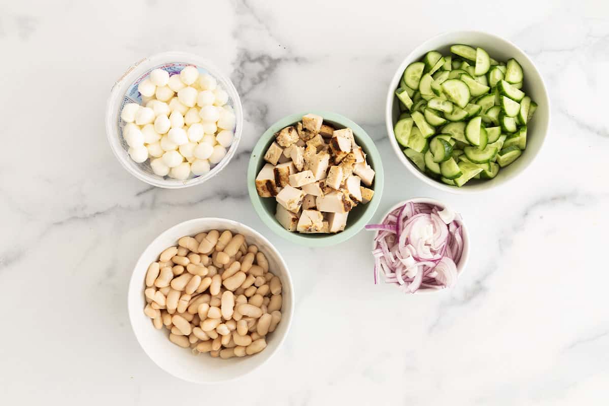 Mix ins for pasta salad with chicken in various bowls.