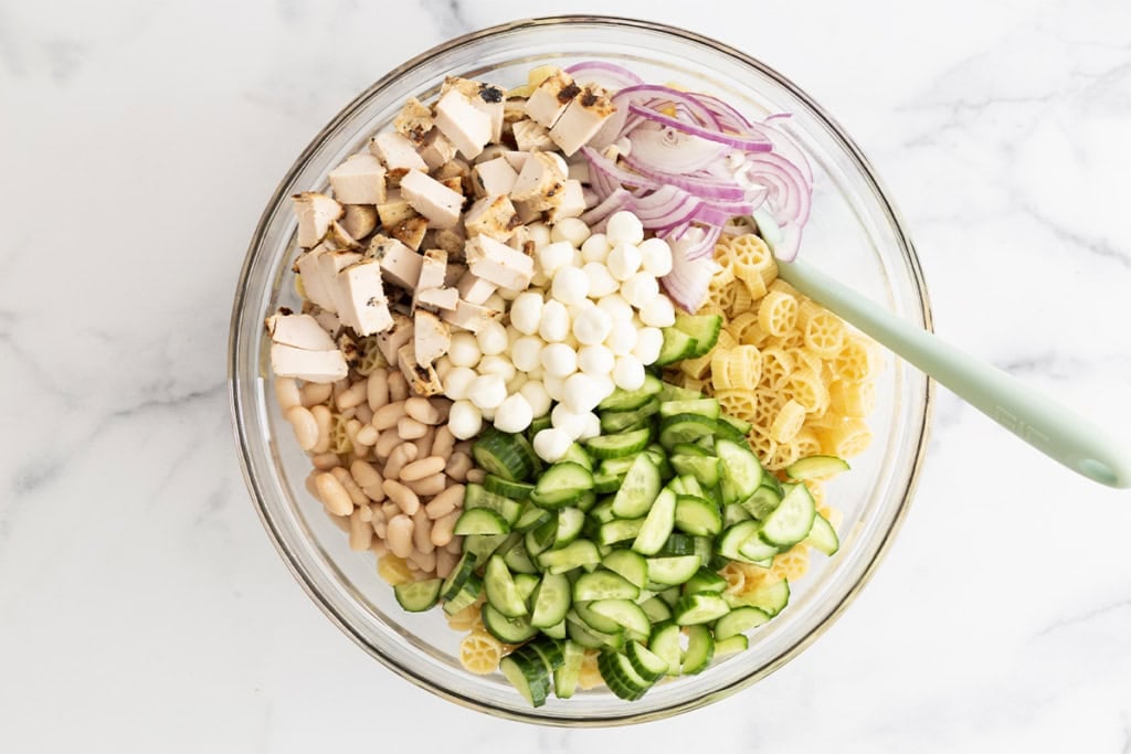 Pasta salad with chicken in glass bowl before mixing.