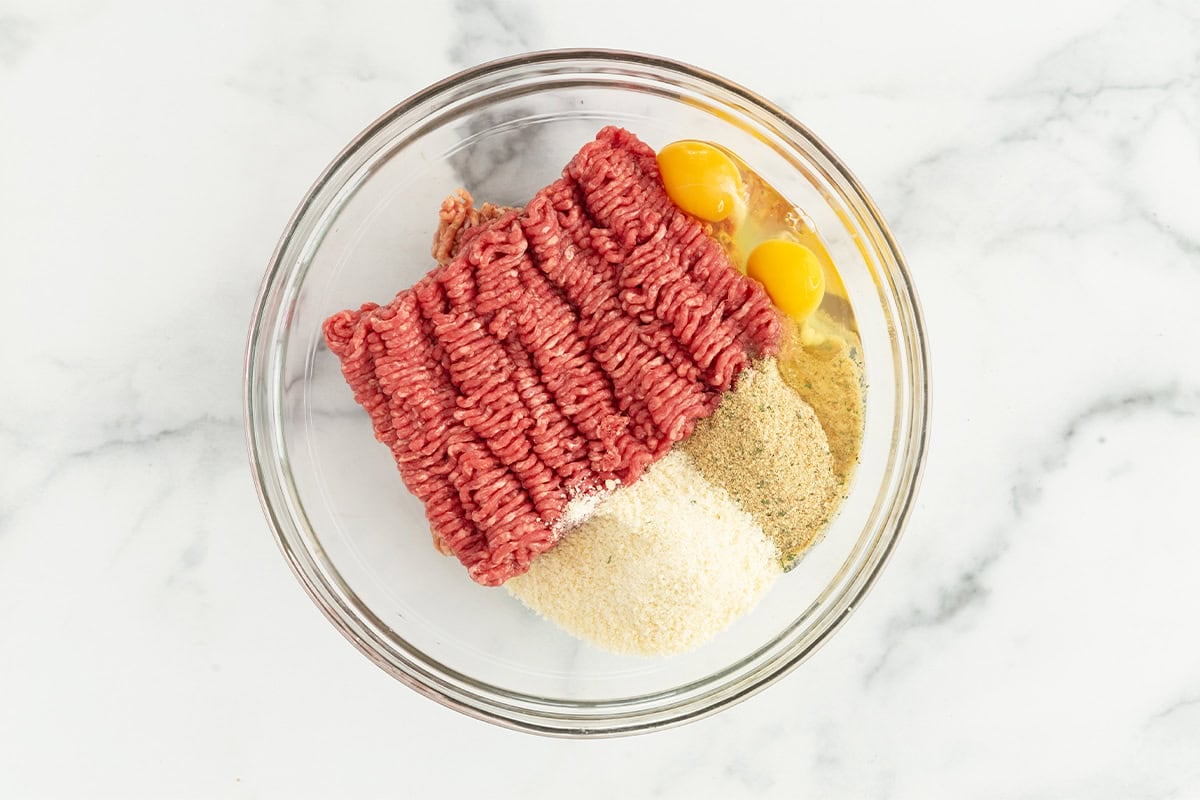 Ingredients for sausage meatballs in glass bowl before mixing. 