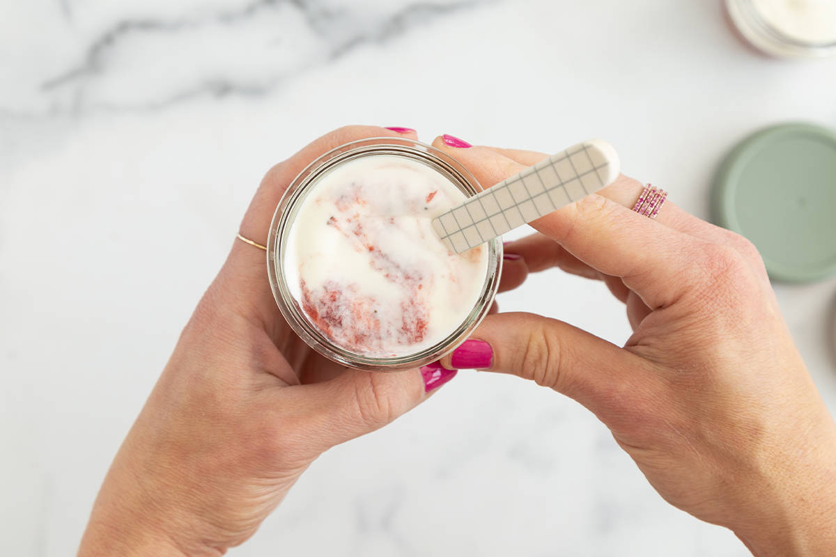 Hands holding glass of strawberry yogurt with spoon.