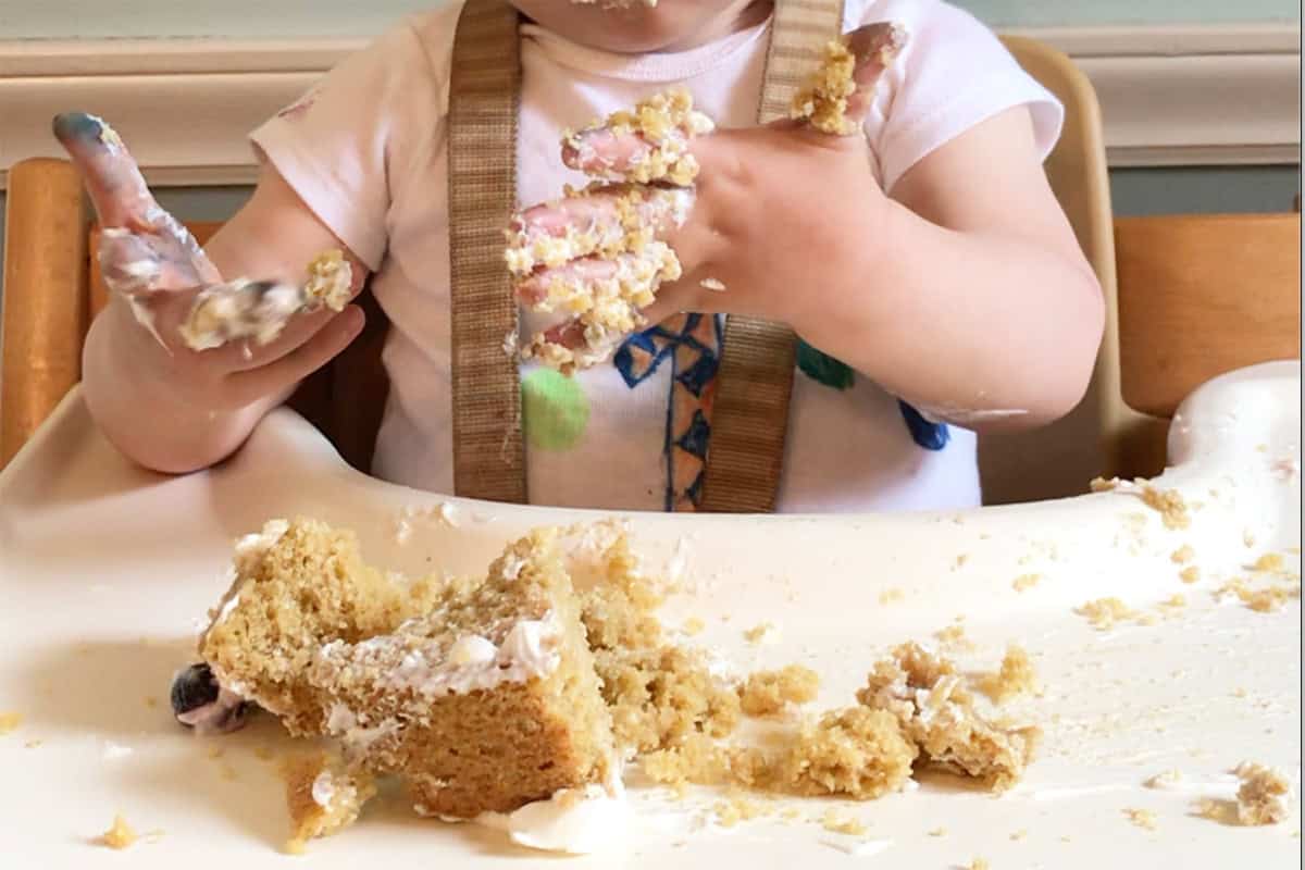 baby with smash cake on hands in highchair.