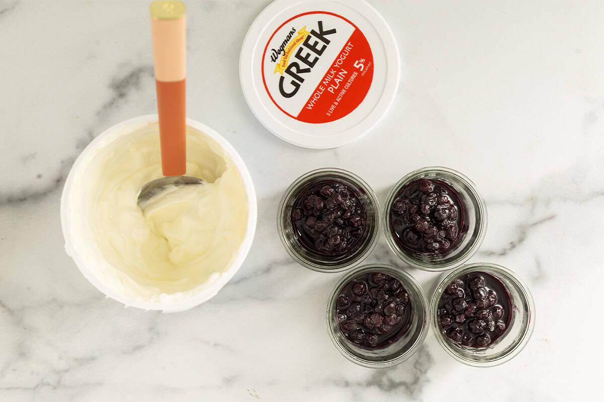 greek yogurt carton with small jars of blueberries on counter.