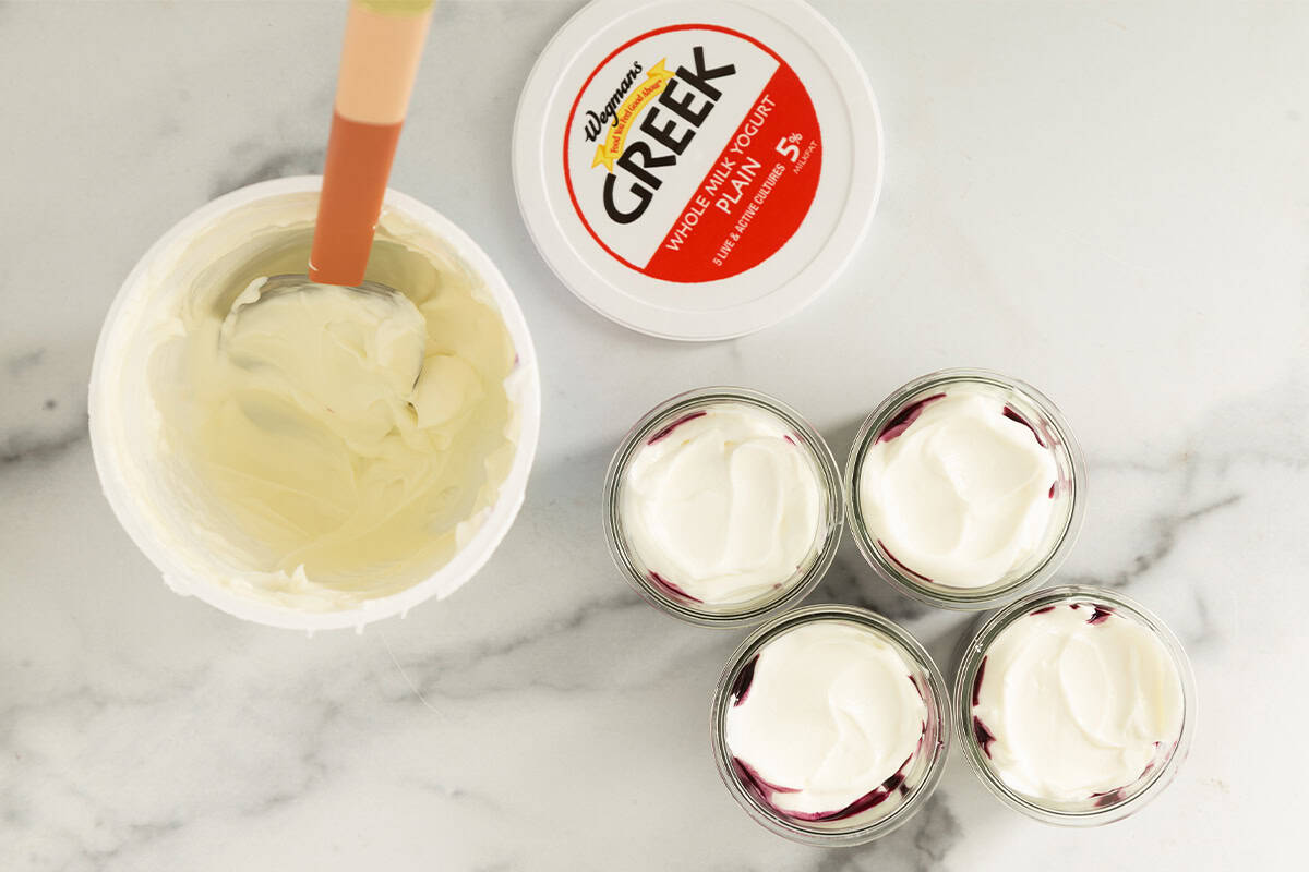 Greek yogurt carton with small jars of blueberry yogurt on counter.
