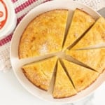 Greek yogurt cake on white plate cut into slices with yogurt container on side.