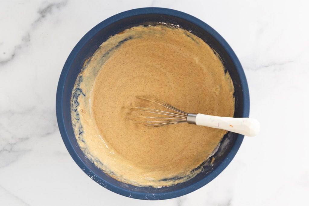 Batter for pumpkin protein pancakes in blue bowl with whisk.
