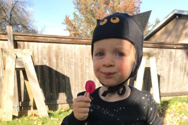 toddler in bat hat with lollipop.