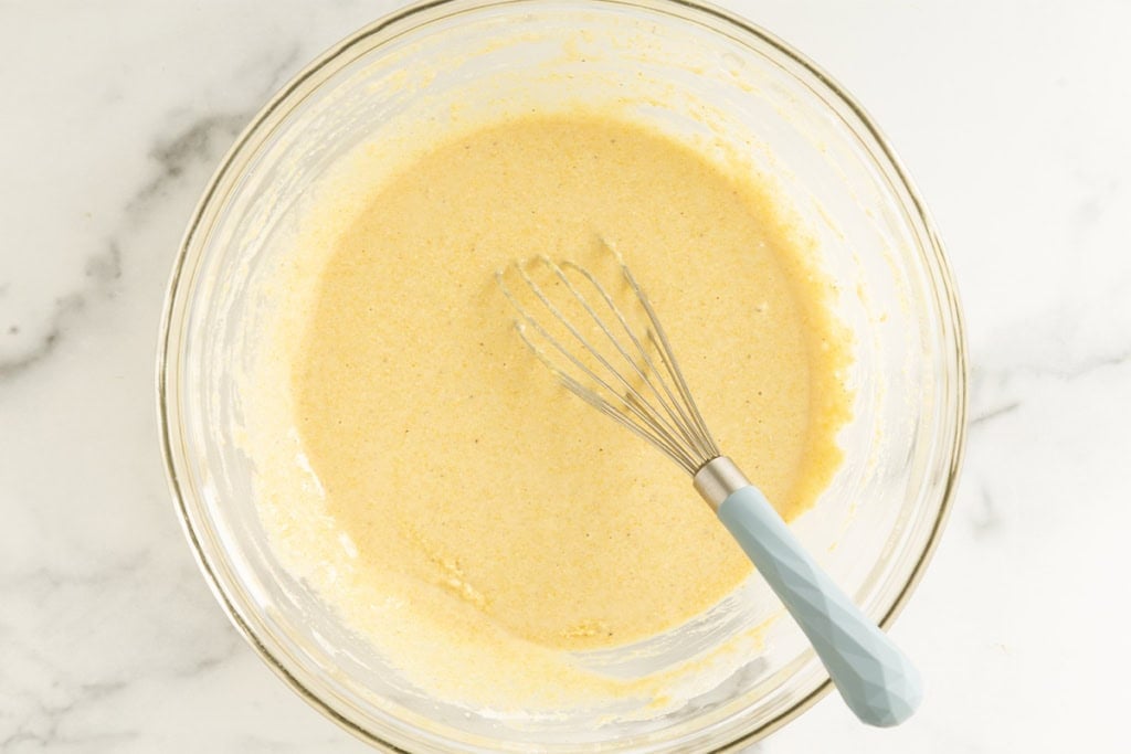 Batter for cornbread muffins with whisk in glass bowl.