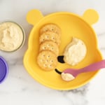 Baby hummus on plate with spoon and crackers.