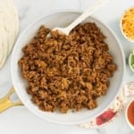 Taco meat in pan with taco supplies on side.