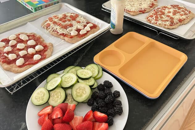 pizza with plate of produce on counter.