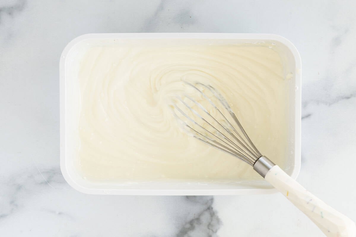 ingredients for vanilla frozen yogurt in container with whisk.
