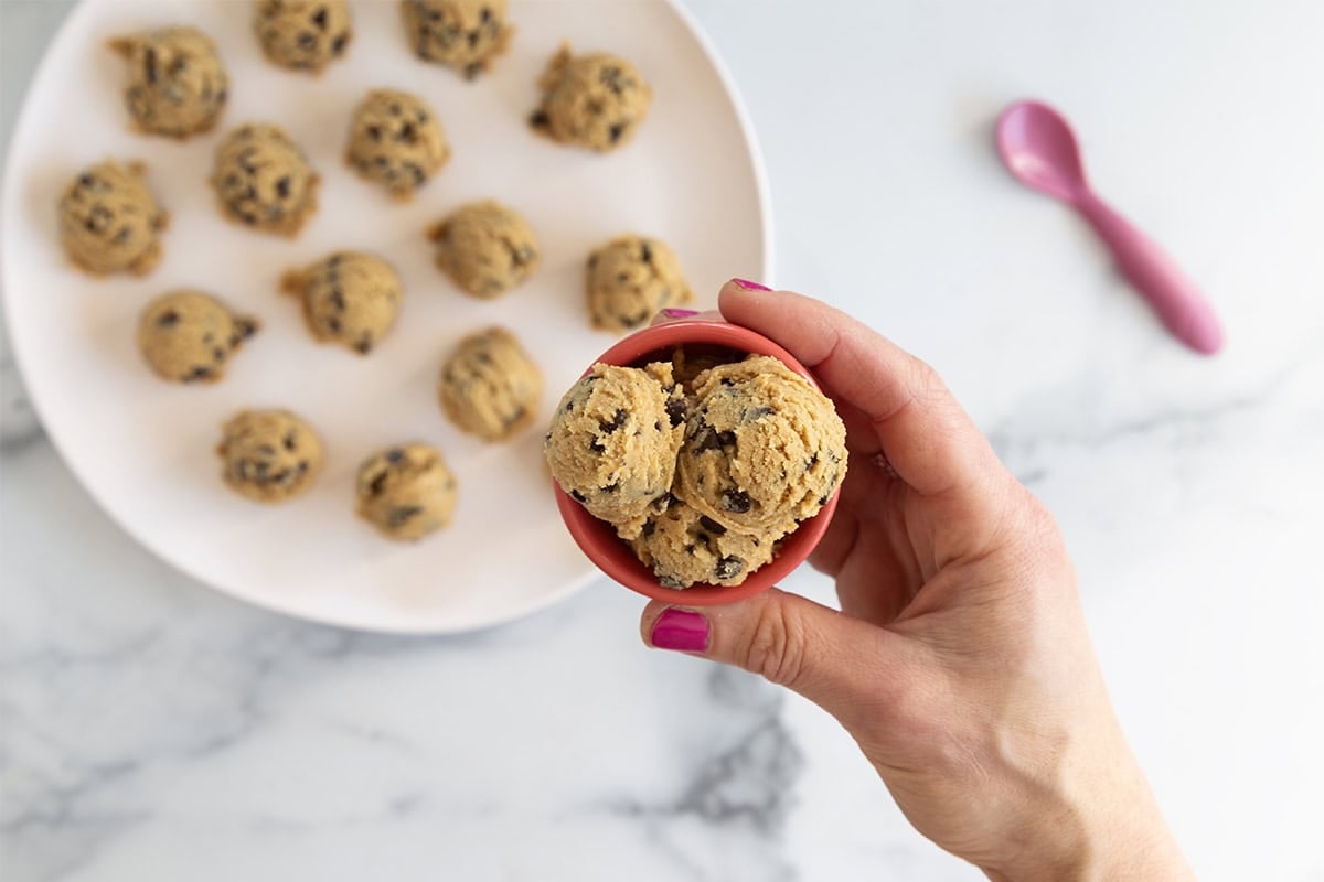 Hands holding pink bowl of edible cookie dough.