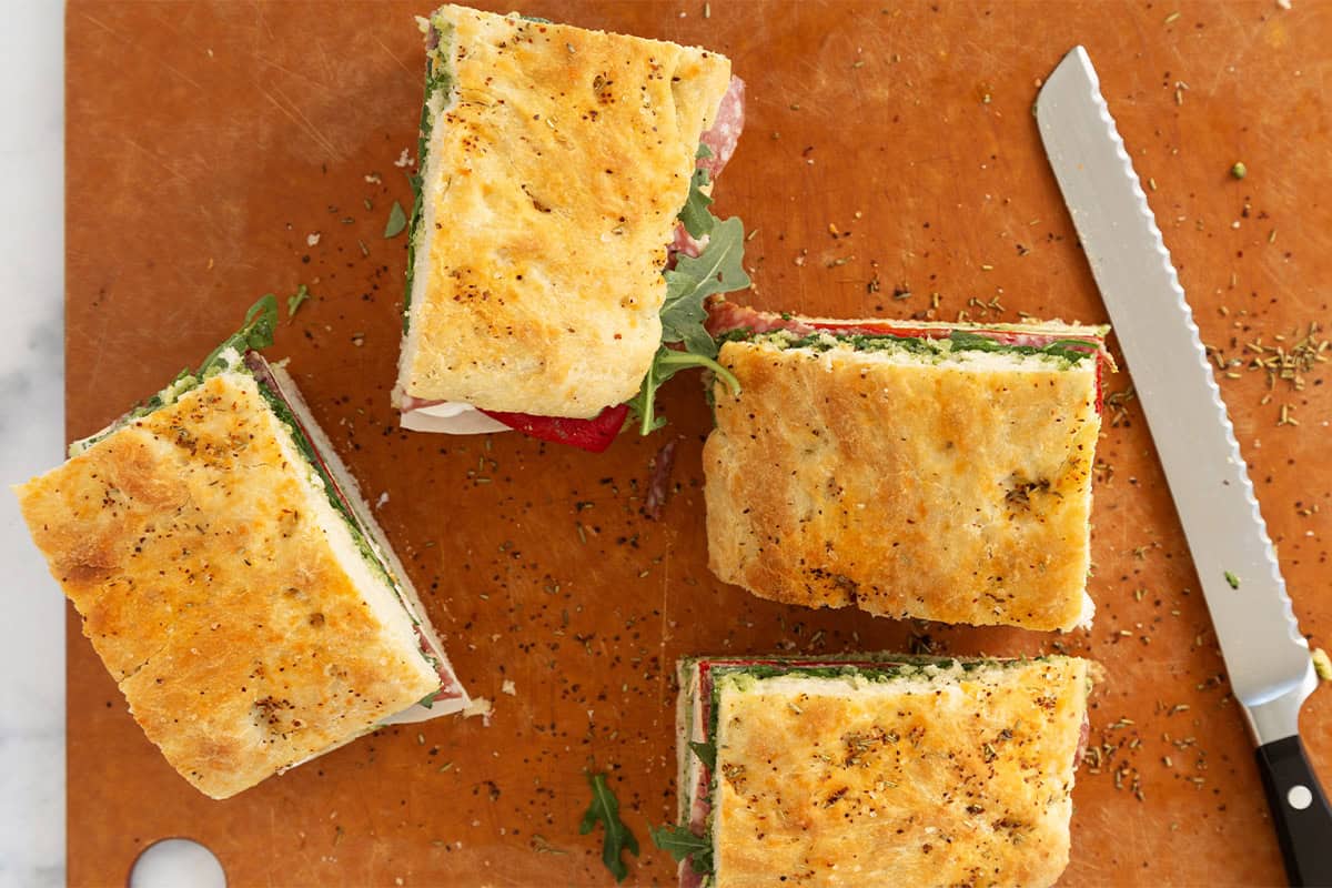 focaccia sandwich slices on cutting board with serrated knife.
