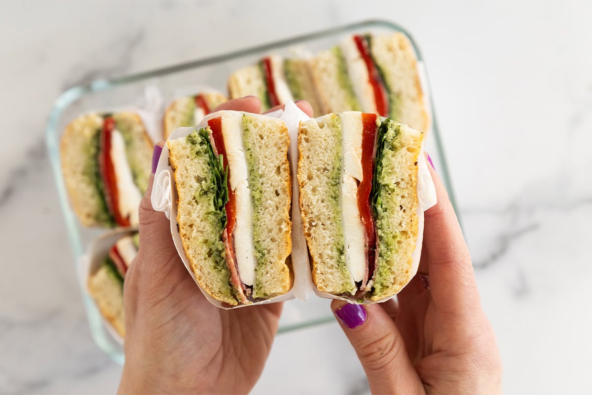 hands holding focaccia sandwich wrapped in parchment paper.