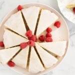 Ricotta cake on plate with frosting and raspberries.