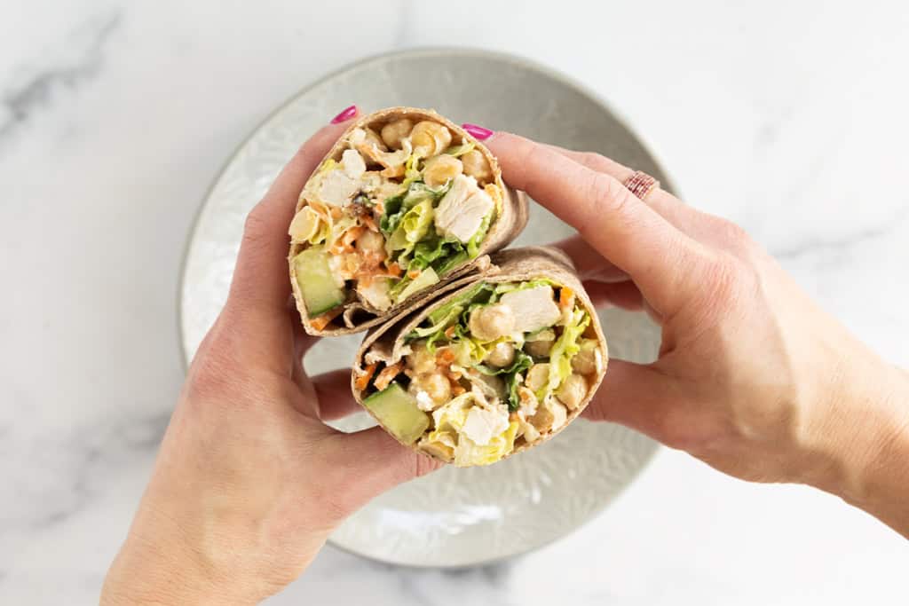 Hands holding salad wrap that is cut in half.