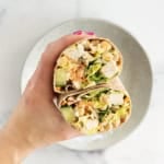 Hands holding salad wrap that is cut in half.