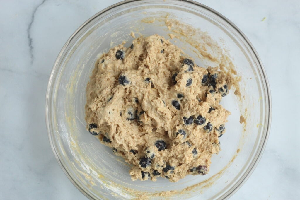 batter for lemon blueberry muffins with berries in a bowl.