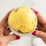 Hands holding bowl of mango frozen yogurt.