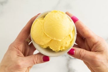 Hands holding bowl of mango frozen yogurt.