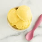 Bowl of mango frozen yogurt with pink spoon on side.