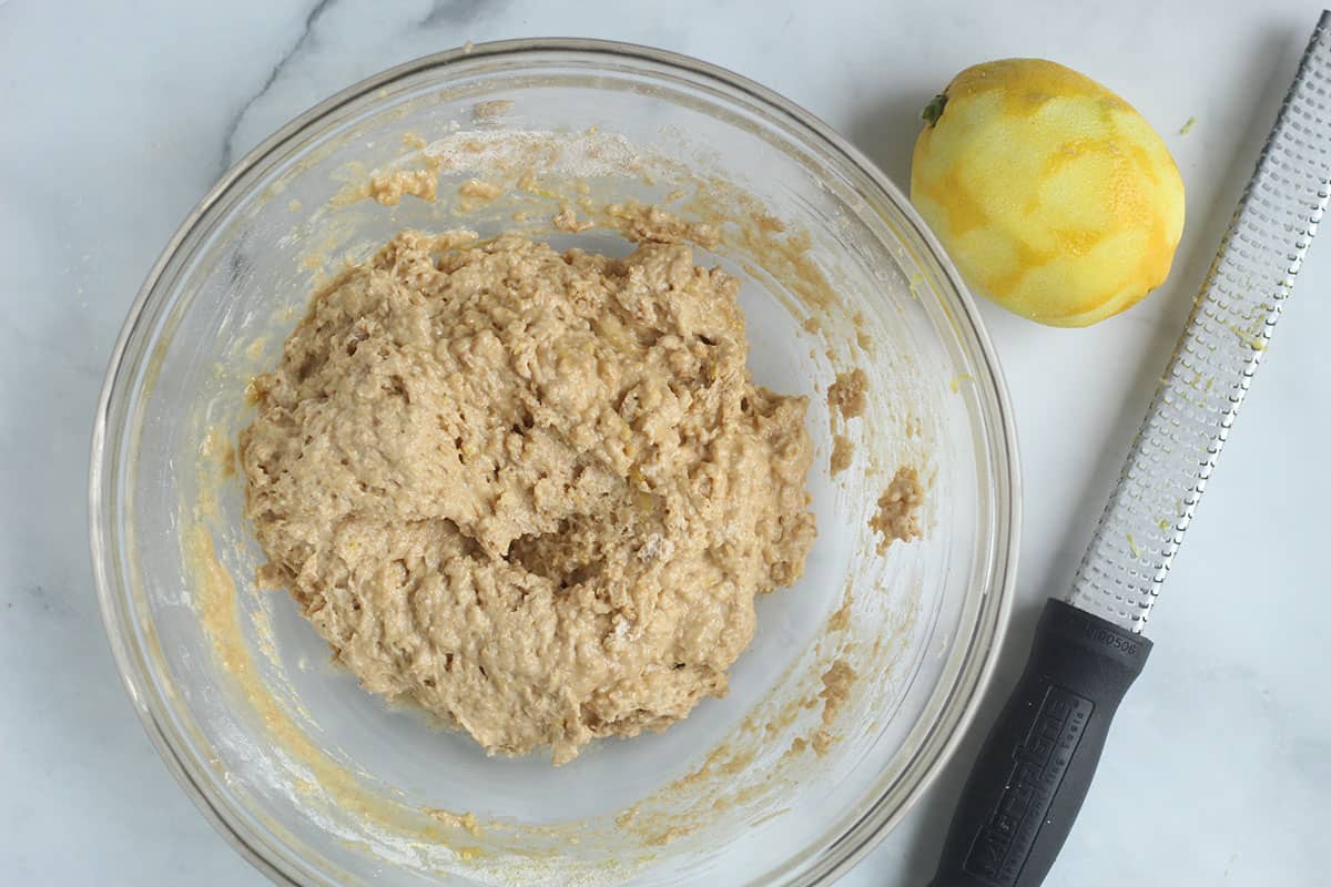batter for lemon blueberry muffins in bowl with lemon.