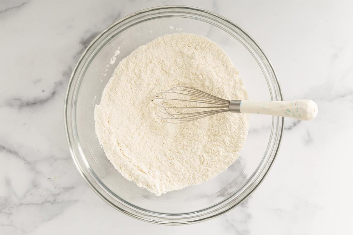 Dry ingredients for cheese muffins in glass bowl with whisk.