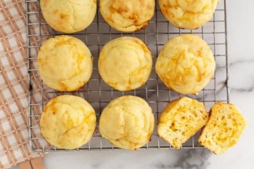 Cheese muffins on cooling rack with one muffin cut in half.