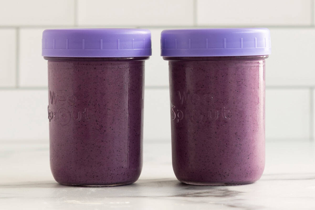 Blueberry smoothie in two glass cups with lids.