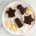 Chocolate banana popsicles on white plate with banana slices.