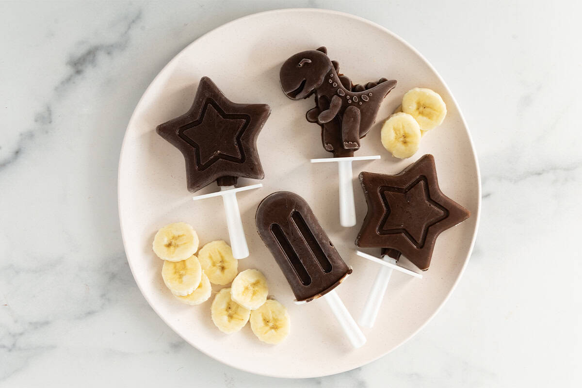 Chocolate banana popsicles on white plate with banana slices. 