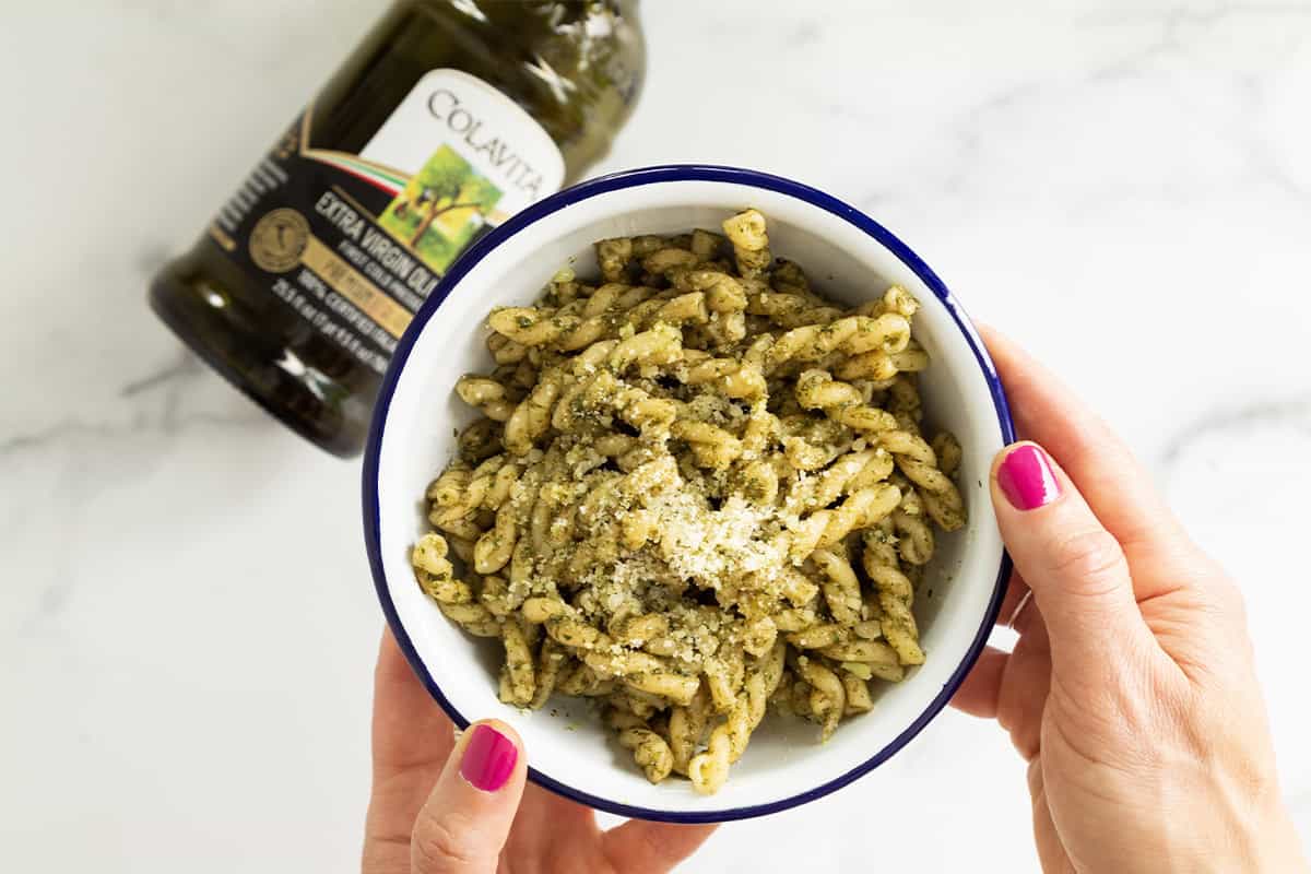 Hands holding bowl of nut free pesto pasta.