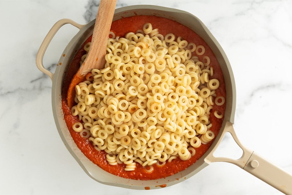 Ring noodles being added to sauce for spaghettios.