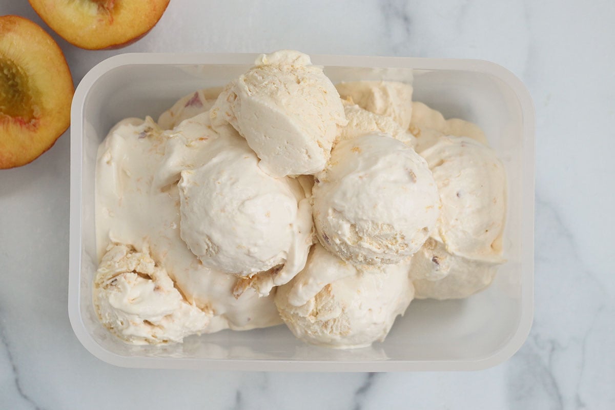 peach ice cream scoops in container with sliced peach.