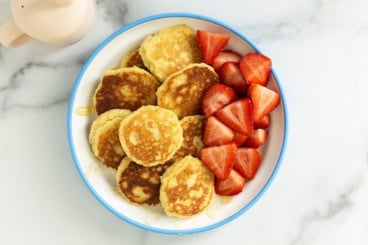 Almond flour pancakes on plate with strawberries and syrup.