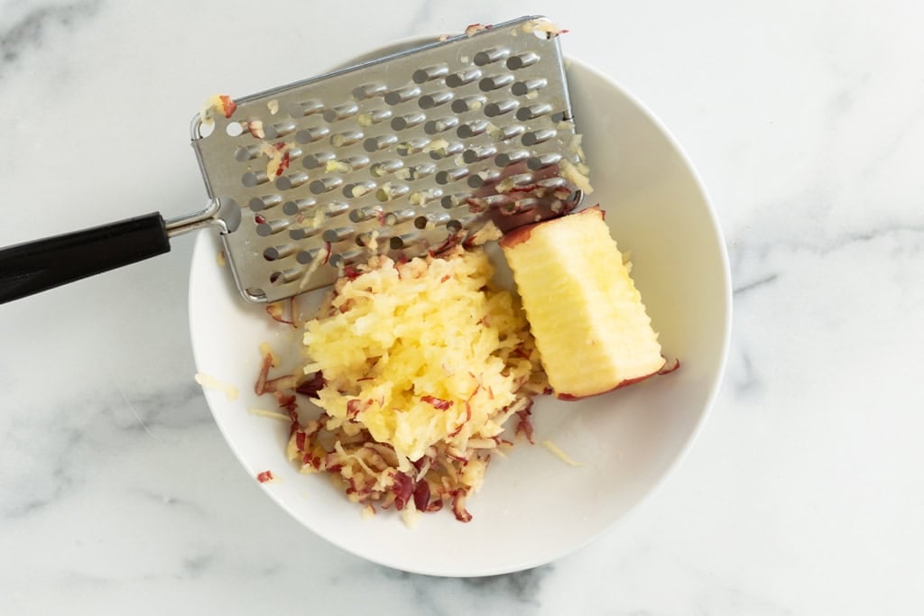 Apple being shredded into bowl.