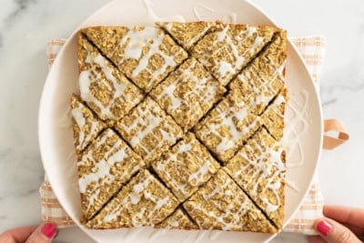 Hands holding white plate with apple oatmeal bars.