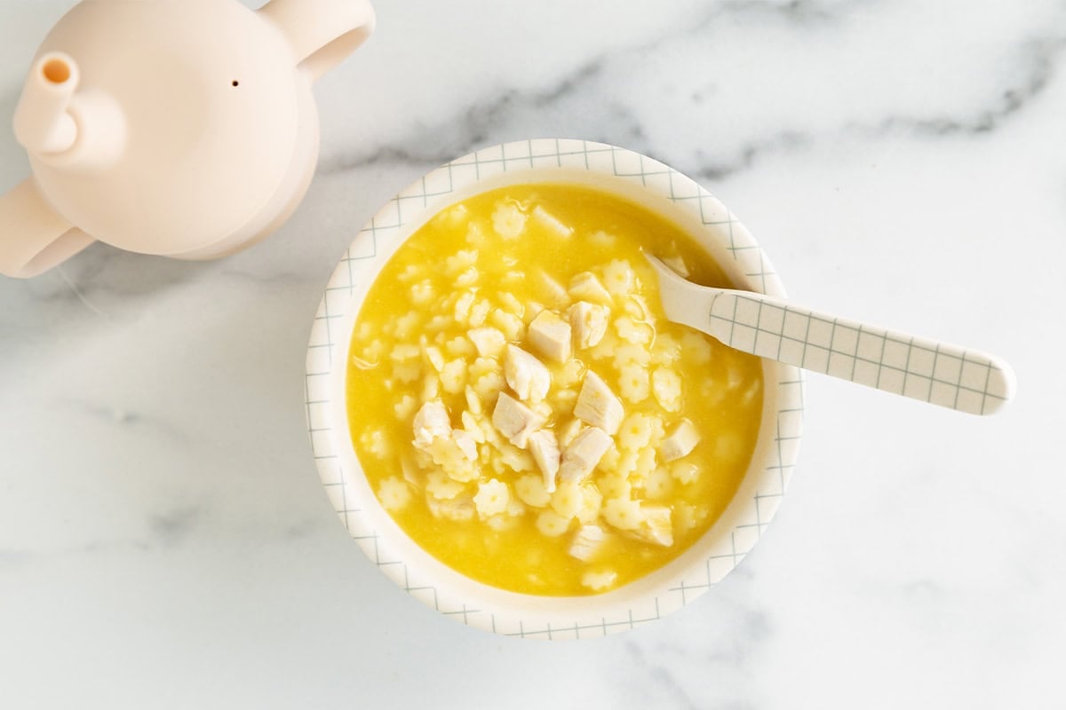 White bowl with baby soup with spoon.